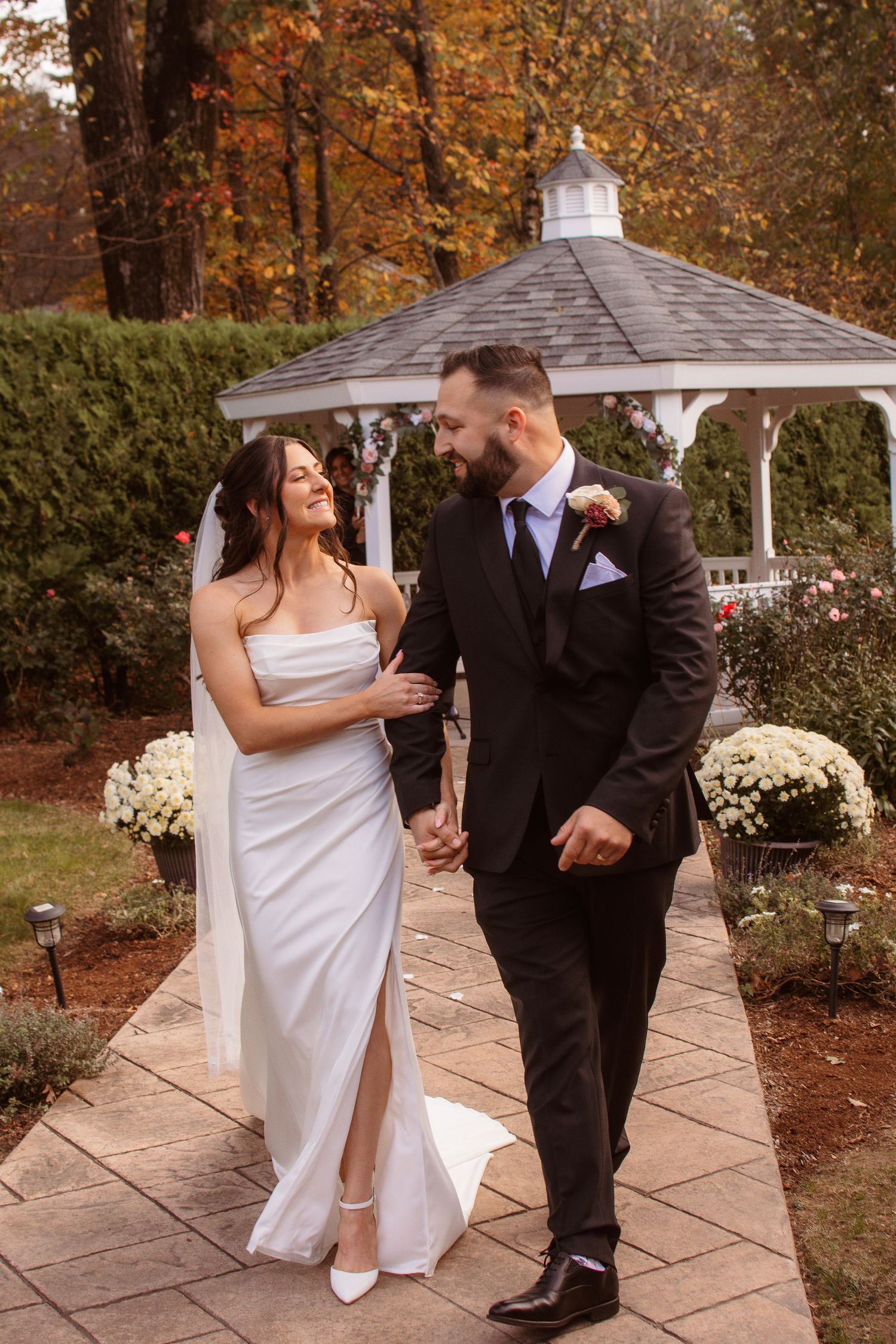 Newlyweds share playful moments on a stone patio with autumn scenery and white gazebo.