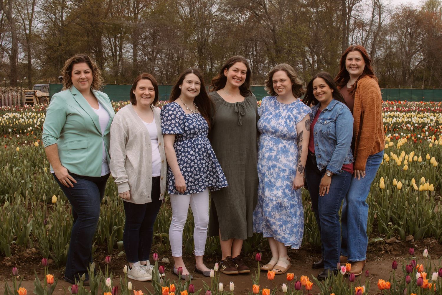 Seven women smiling together in a colorful tulip field during spring.