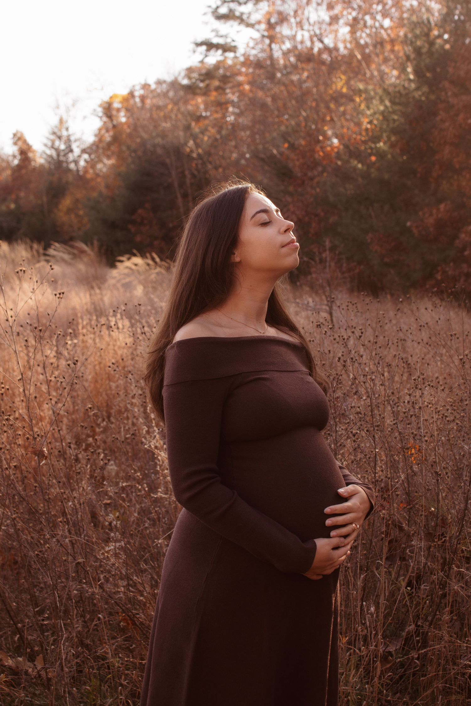 Autumn outdoor portrait of someone in a brown sweater standing among tall dried grass at golden hour.