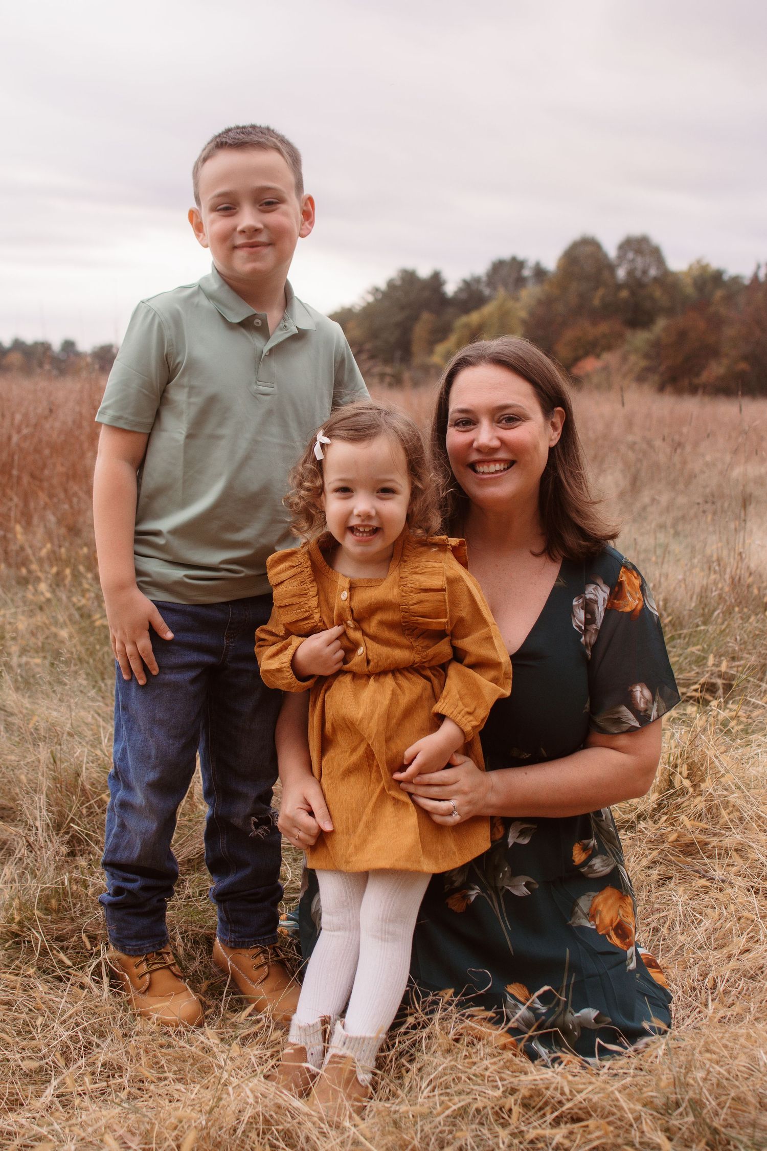 A family sits together in a rustic autumn field wearing coordinating earth-toned outfits for outdoor portraits.