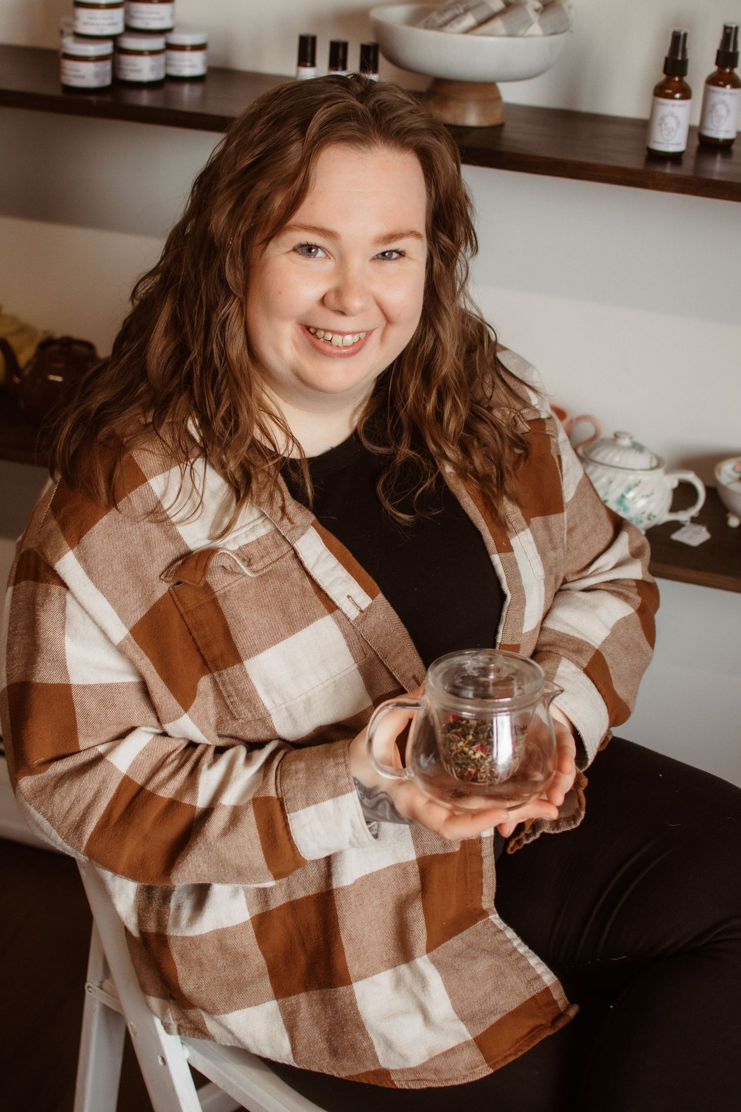 Someone in a brown plaid flannel shirt holds a glass jar while standing in a retail shop with shelving in the background.