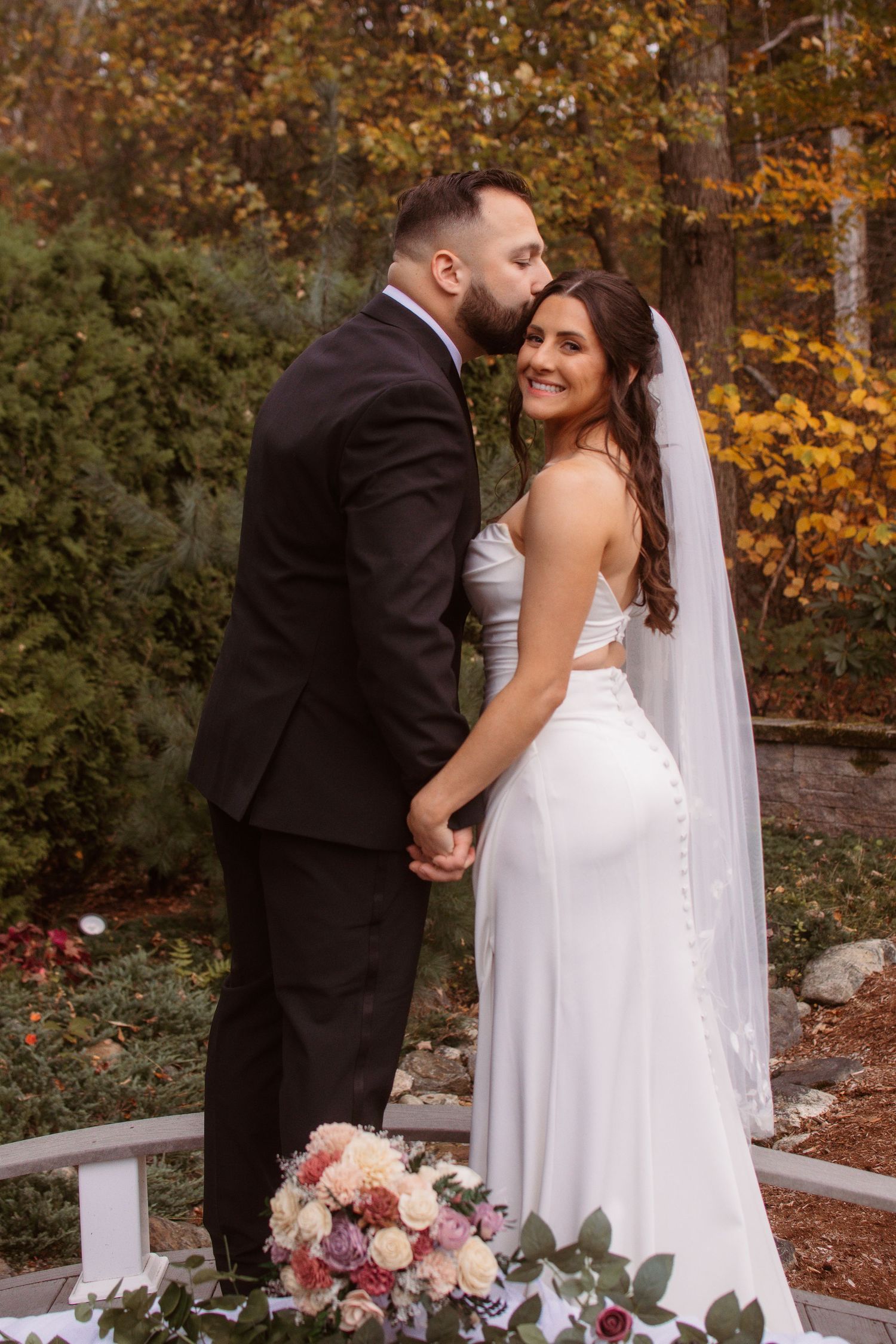 Wedding couple shares intimate moments by white gazebo with autumn colors and floral decorations.