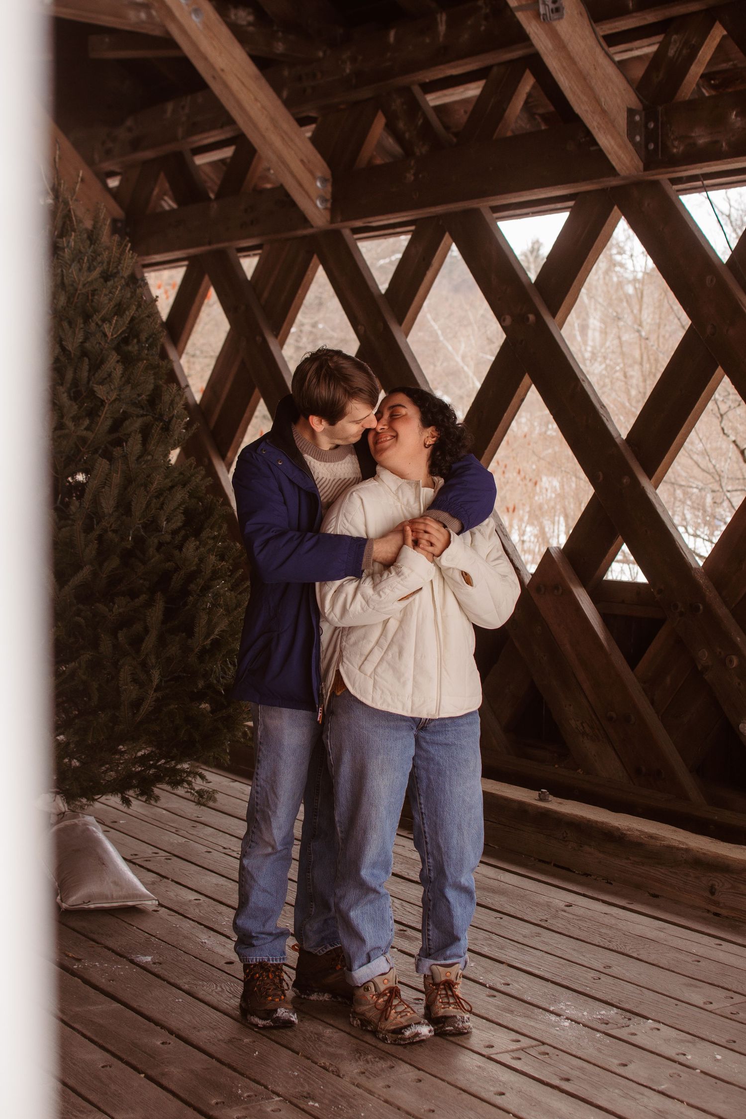 A couple shares an intimate moment together on a wooden covered bridge during winter.