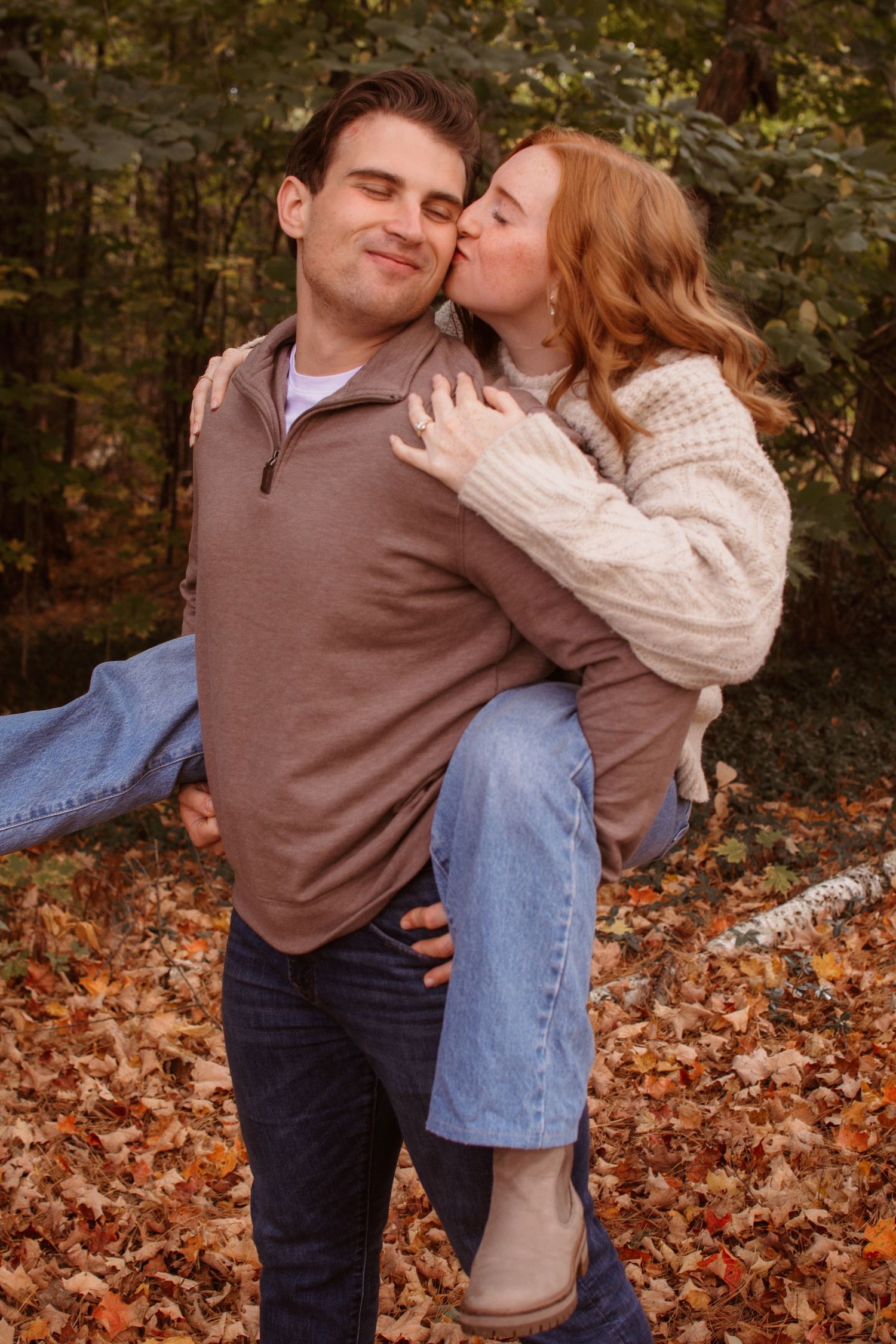 A couple shares romantic kisses while standing in autumn leaves during a fall outdoor photo session.
