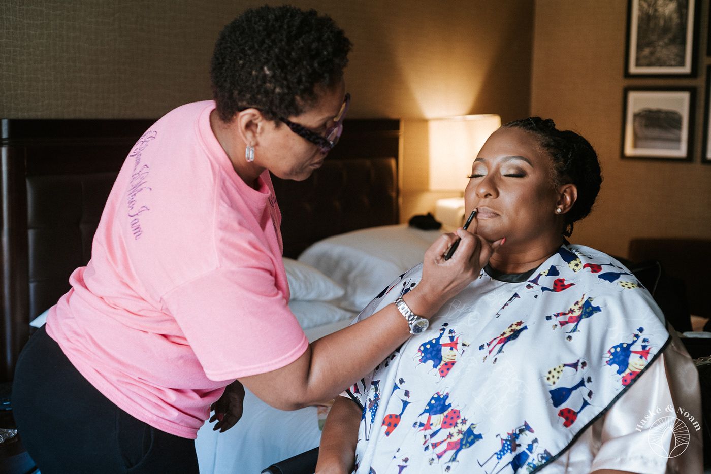 Makeup artist applying cosmetics to someone wearing a floral robe during wedding preparations.