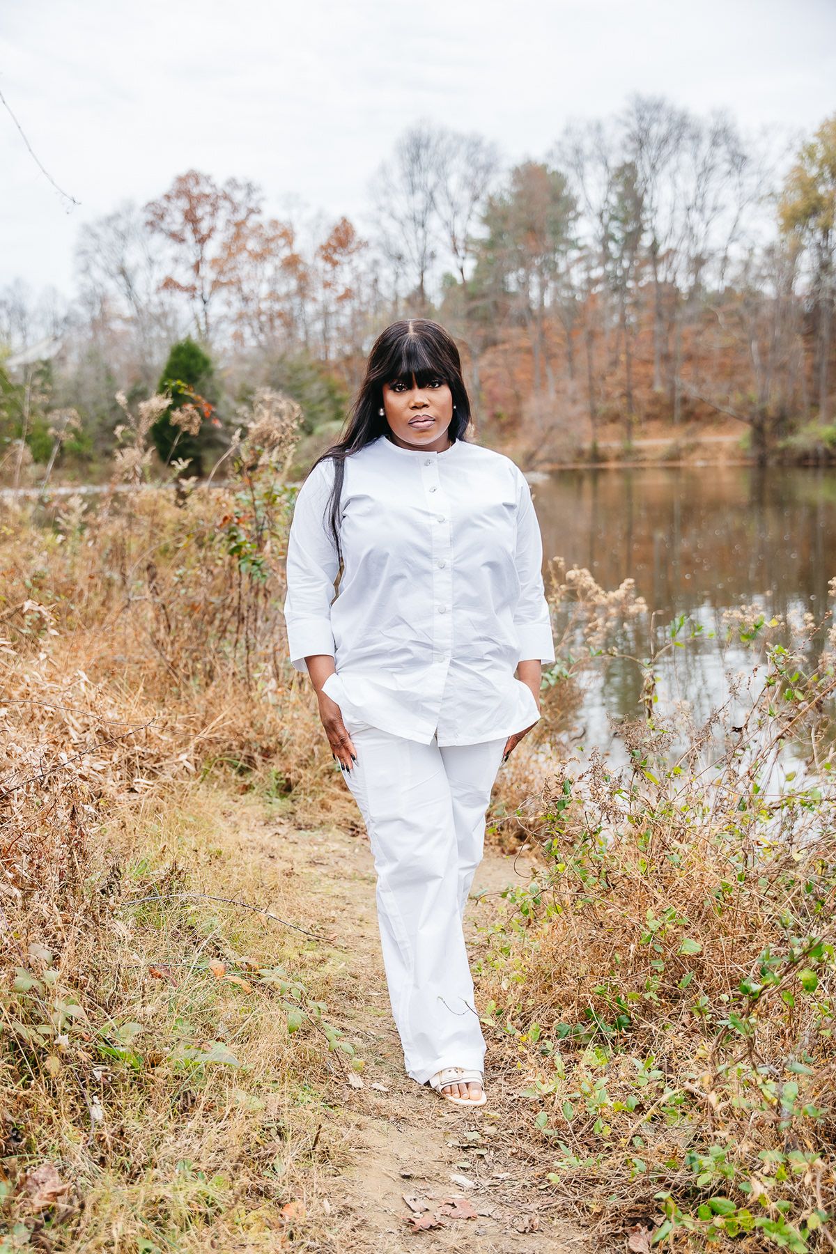 Person in all-white outfit walking along scenic lakeside path during autumn.