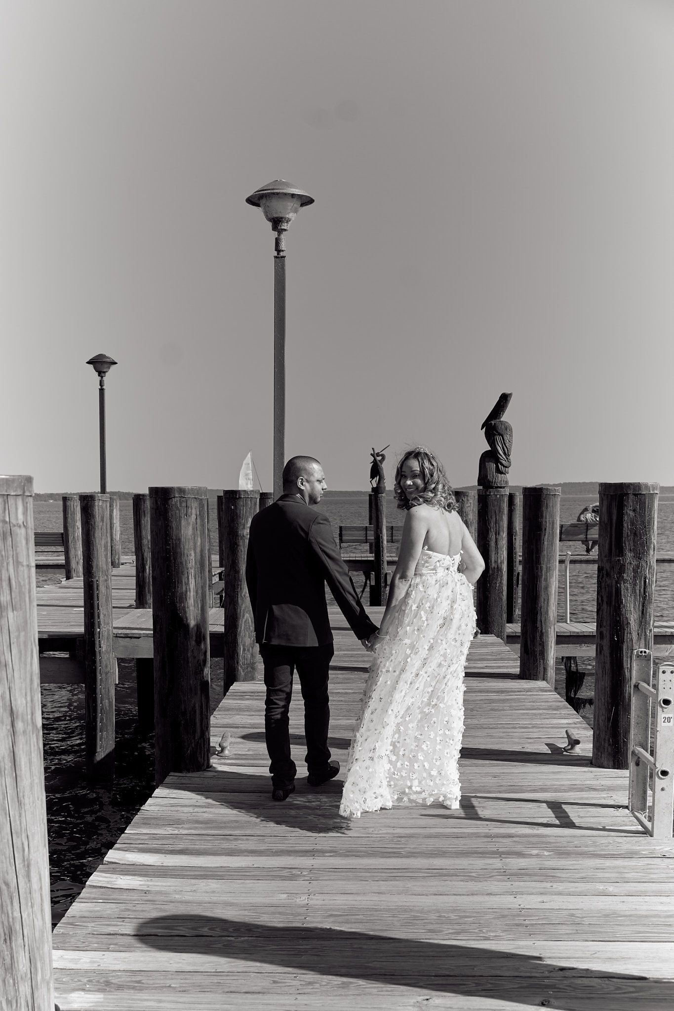 A black and white photo of a couple walking on a wooden pier.