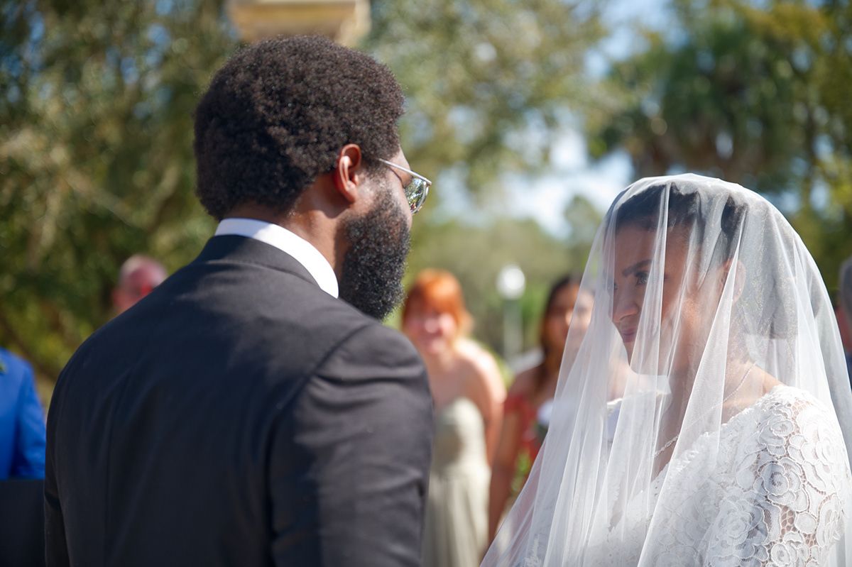 Side view of couple during outdoor wedding ceremony with guests in background.