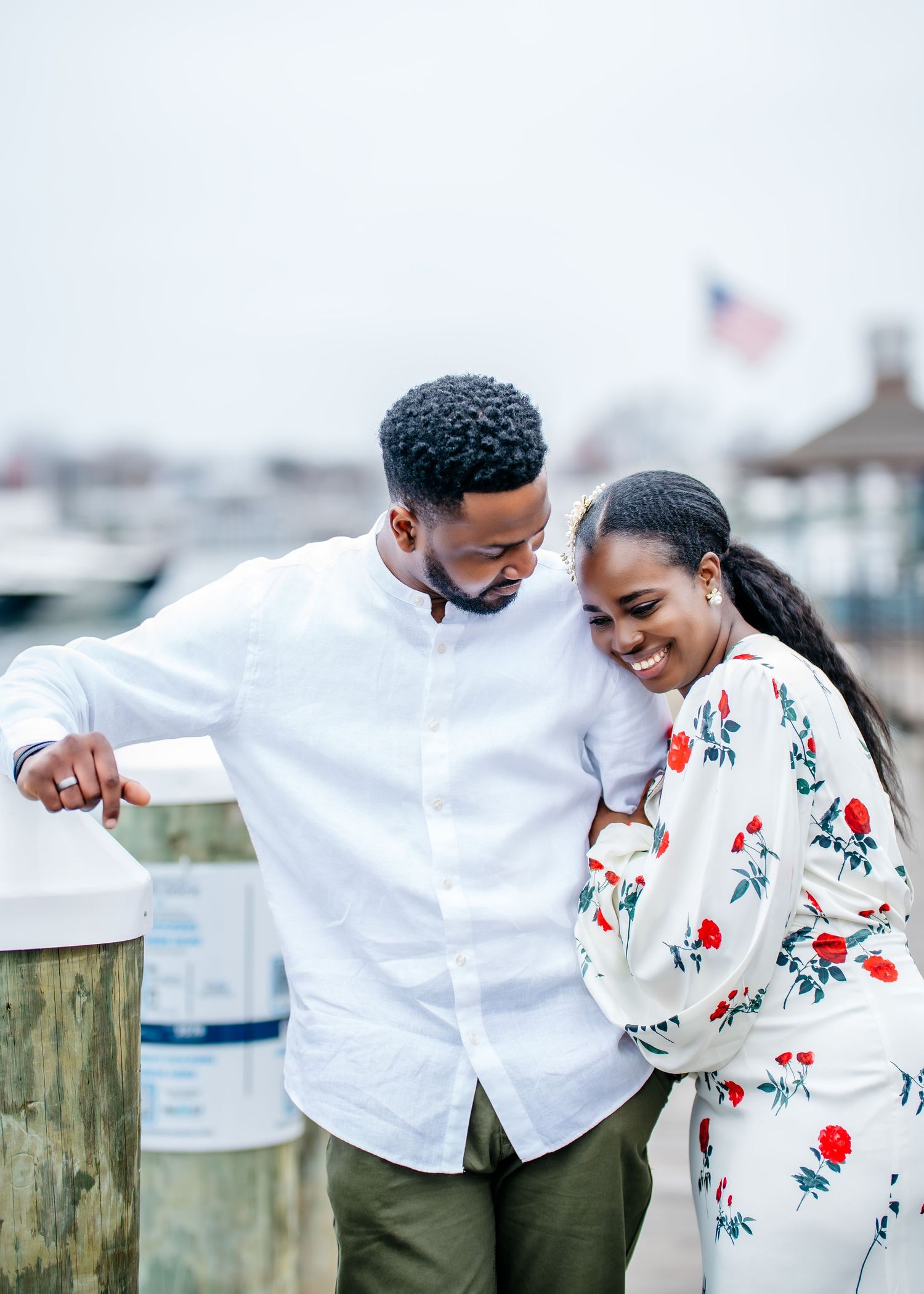 Two people sharing a happy moment together by a marina with boats and an American flag in the background.