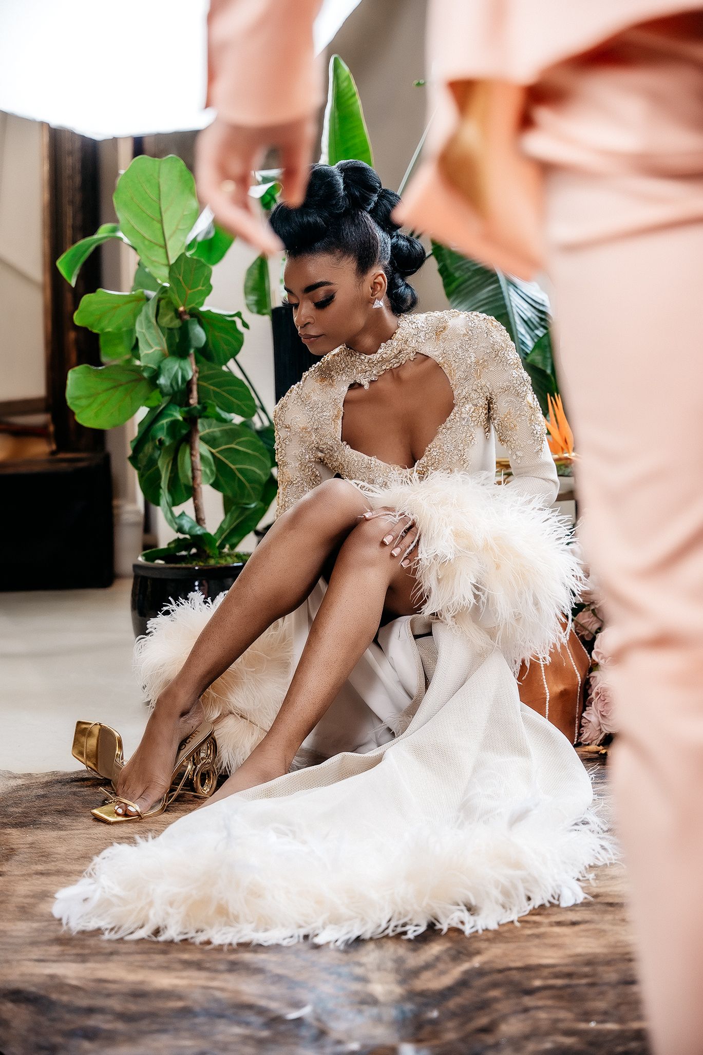 Elegant bridal fashion shot featuring white feathers and gold heels among tropical plants.