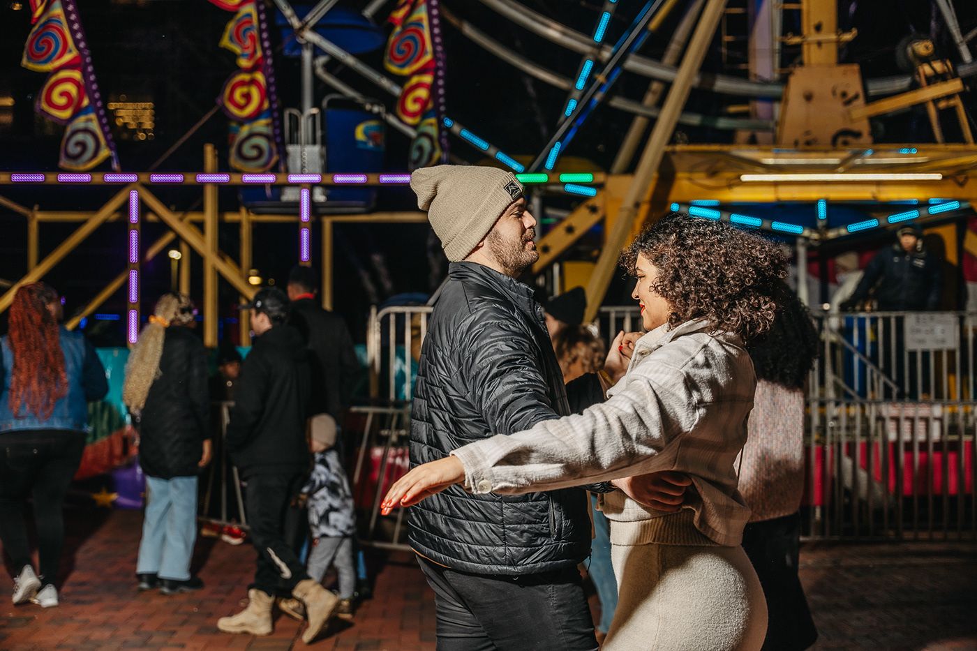 Couple dancing together at a carnival with colorful lights in the background.