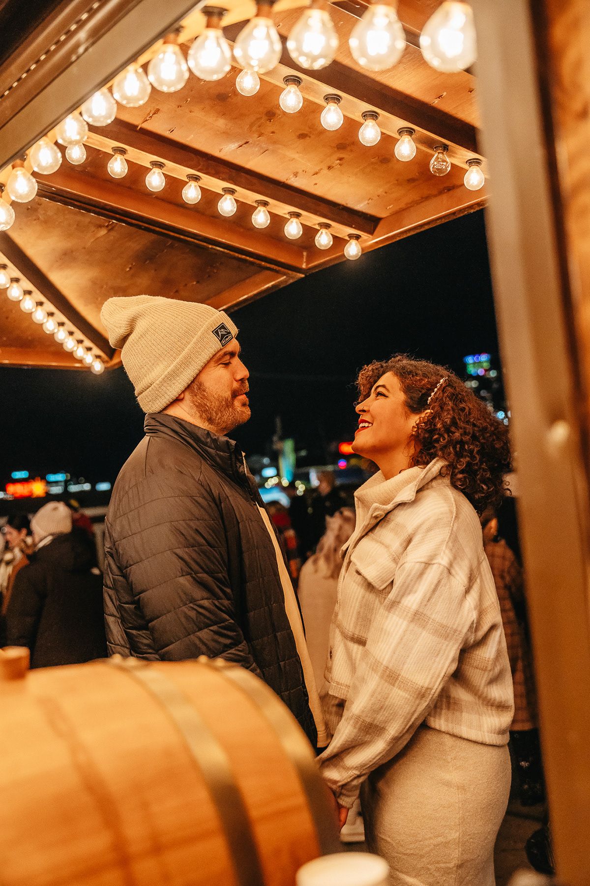 A couple gazes at each other under warm string lights in an evening setting.