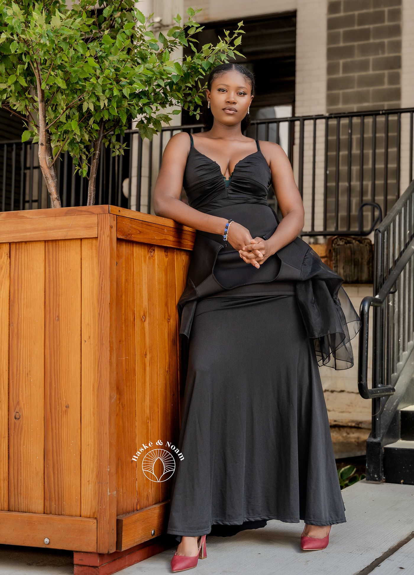 A elegant pose in a black evening gown next to a wooden planter box on an outdoor patio.