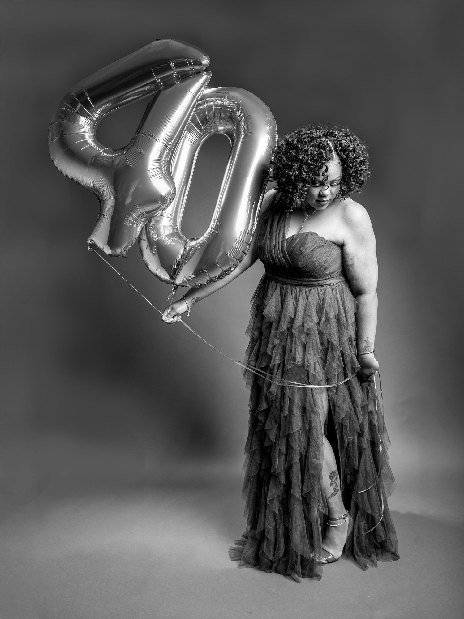 Black and white portrait with a person in a flowing dress holding a large 40 balloon.