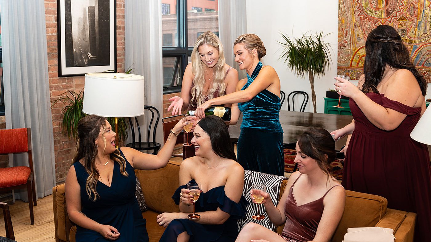 A group of friends celebrating together in formal attire at a pre-wedding gathering in a modern living room.