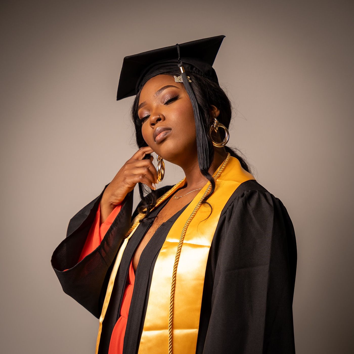 Graduate wearing gold stole and cap poses elegantly in studio setting.