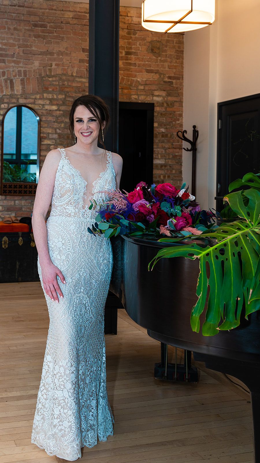 Elegant white lace wedding gown photographed next to vibrant floral arrangement in an industrial-style venue.