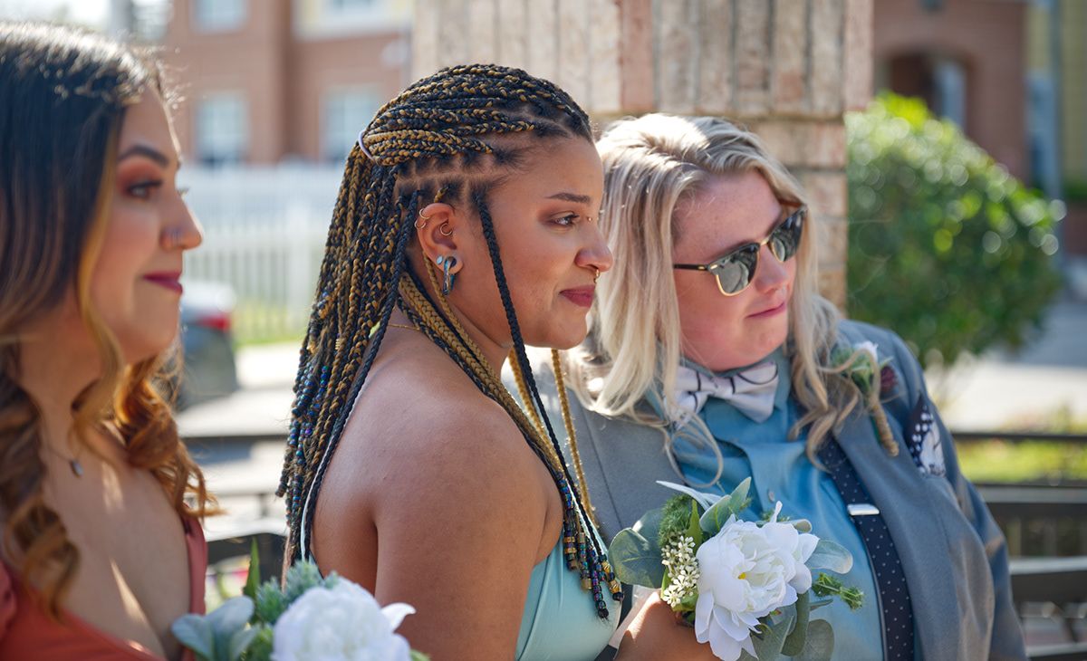 Three wedding attendants stand together outdoors holding white floral bouquets.