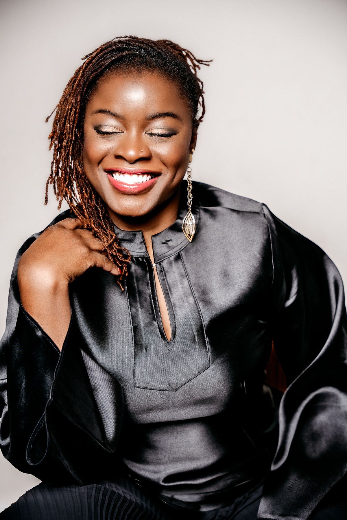 Person wearing a black satin top with braided hair laughing joyfully against neutral background.