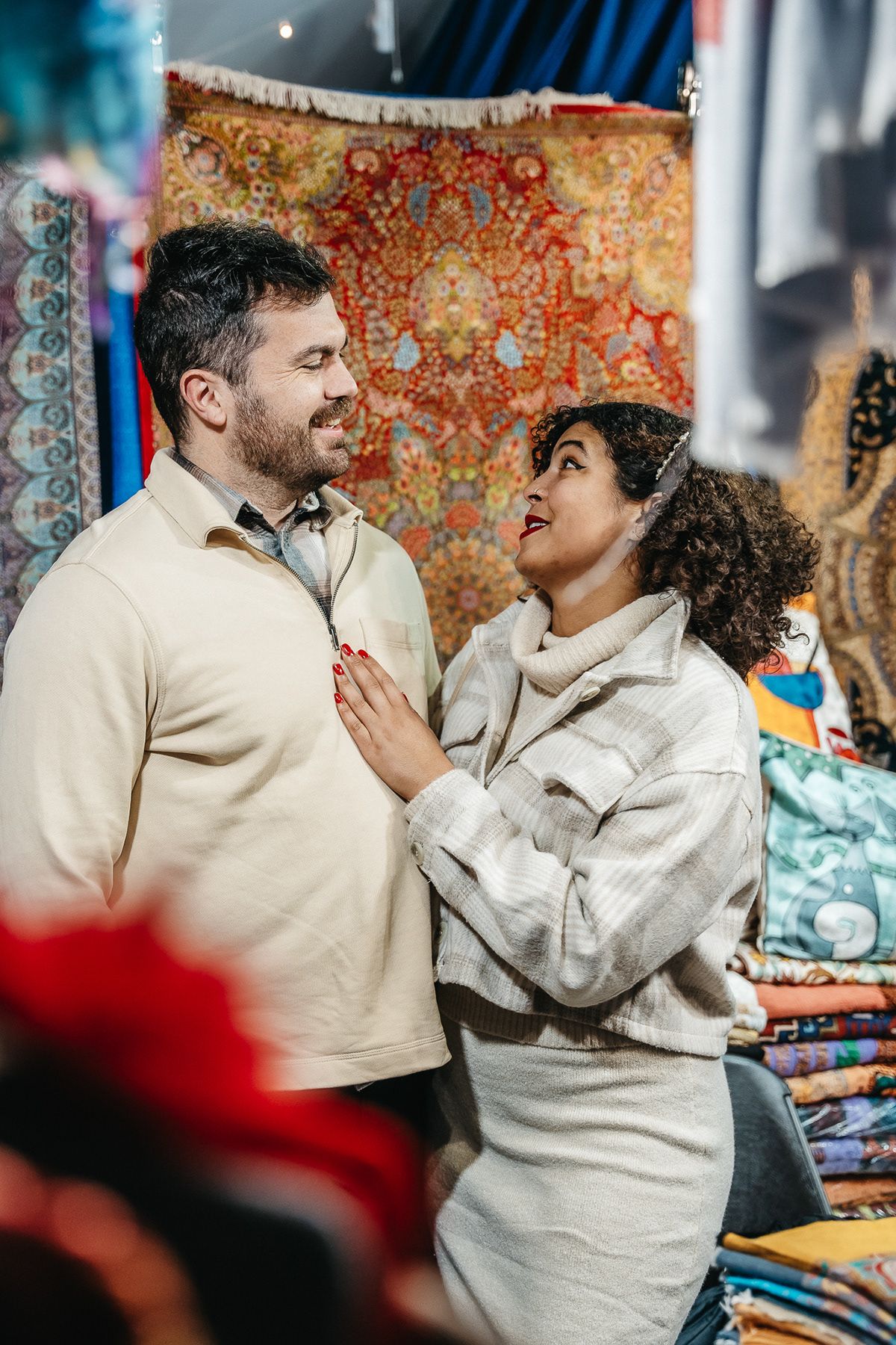 Couple sharing a loving glance while shopping at a market with ornate rugs in the background.