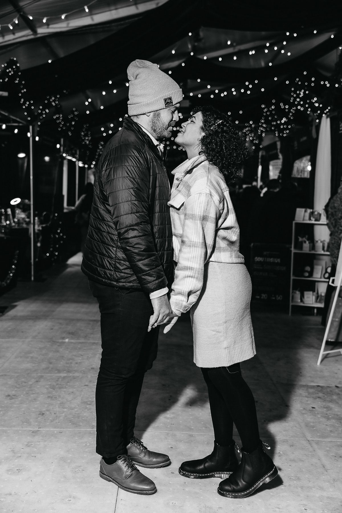 Black and white photo of a couple sharing an intimate moment under string lights.