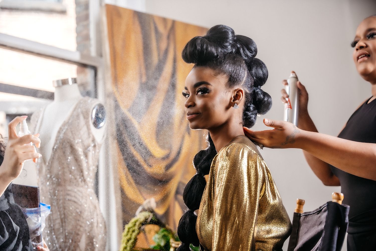 Behind the scenes preparation showing elegant hairstyling in a bright window-lit room.