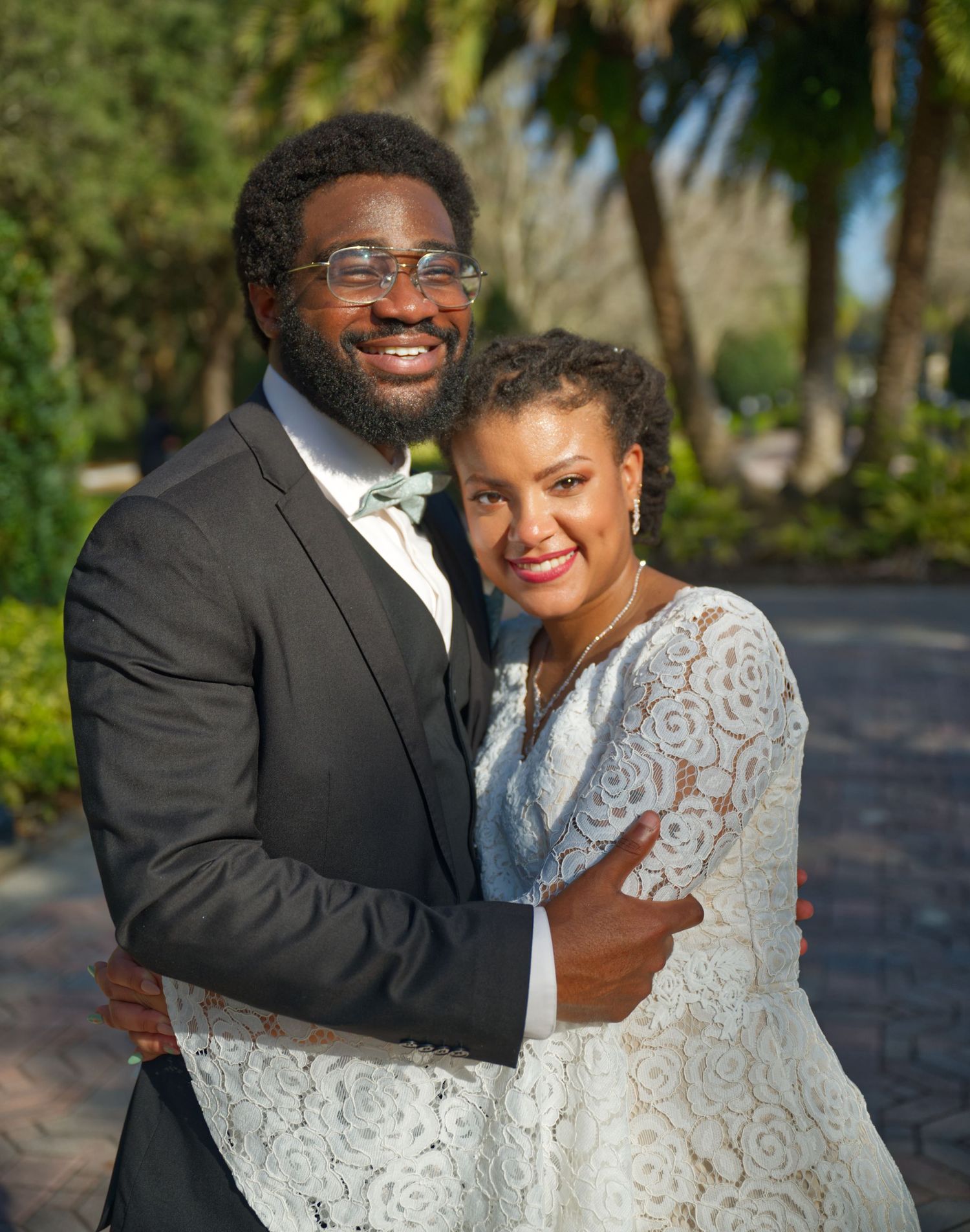 A joyful couple embracing outdoors in wedding attire near palm trees.