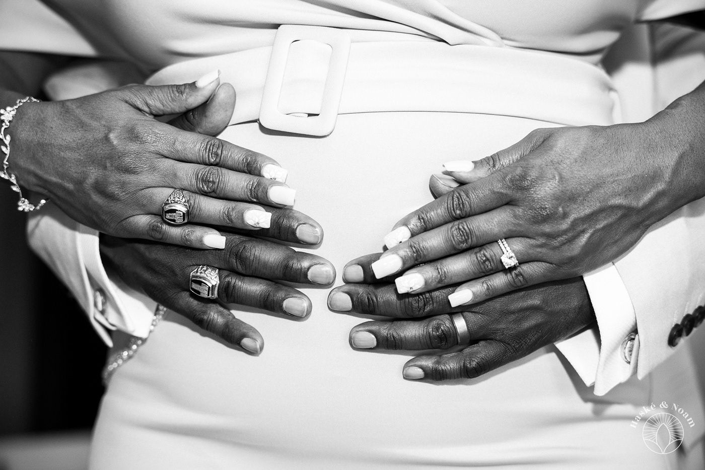 Black and white close-up of hands with rings resting on white fabric.