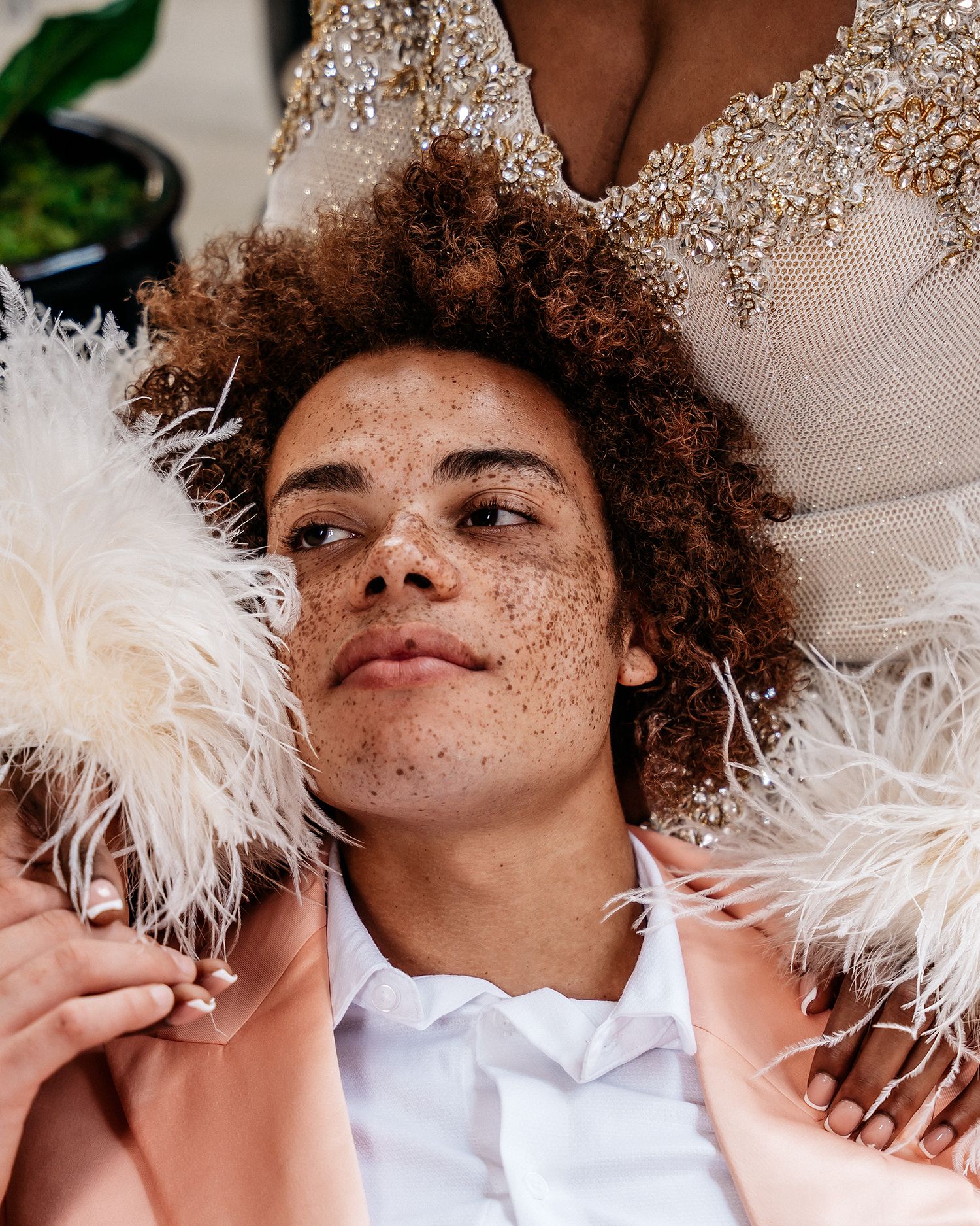 Close-up fashion portrait showcasing natural freckles and feather-adorned clothing.