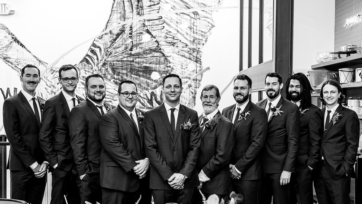Black and white group photo of wedding party in matching dark suits.