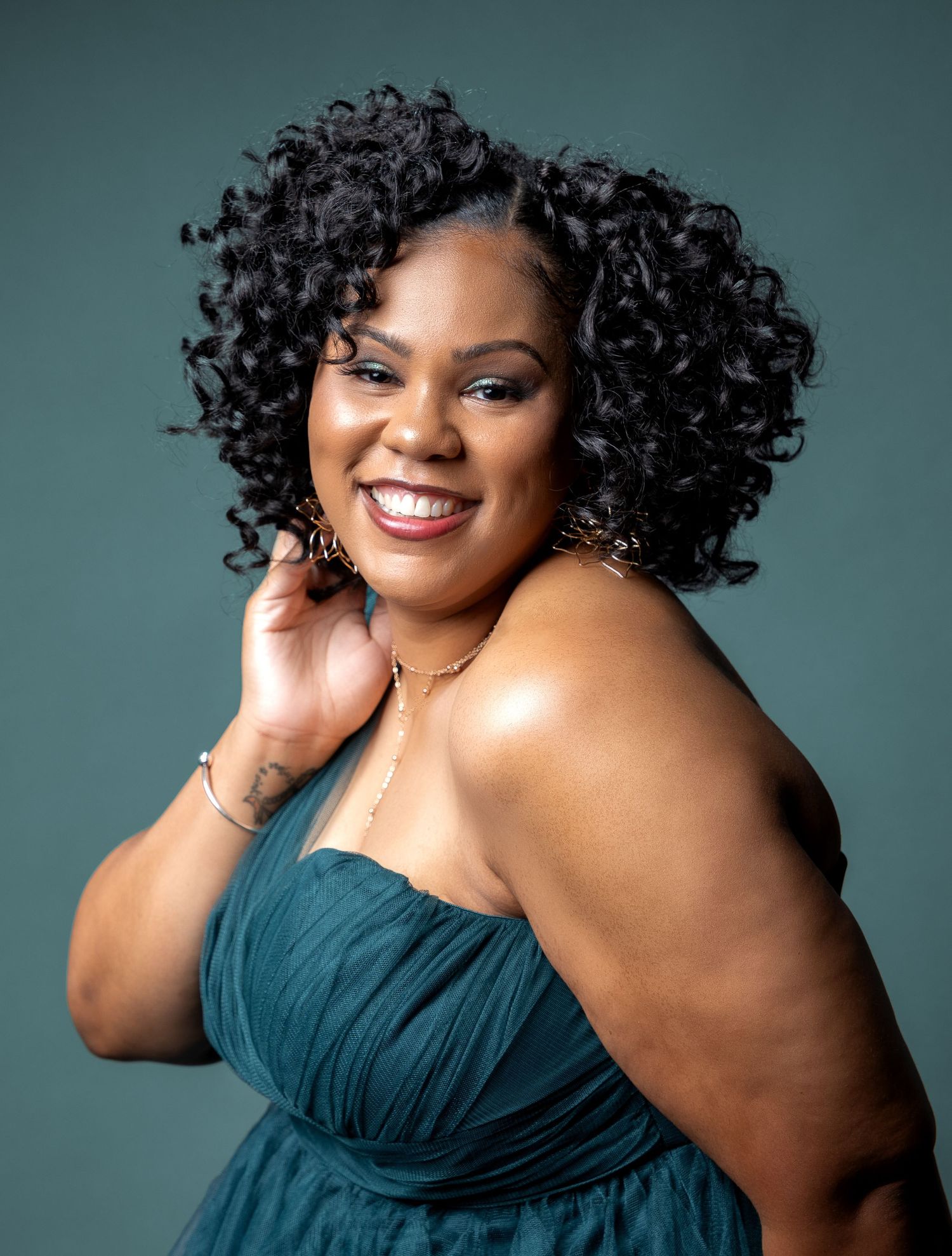 Portrait of person in teal gown with voluminous curly hair against blue-green backdrop.