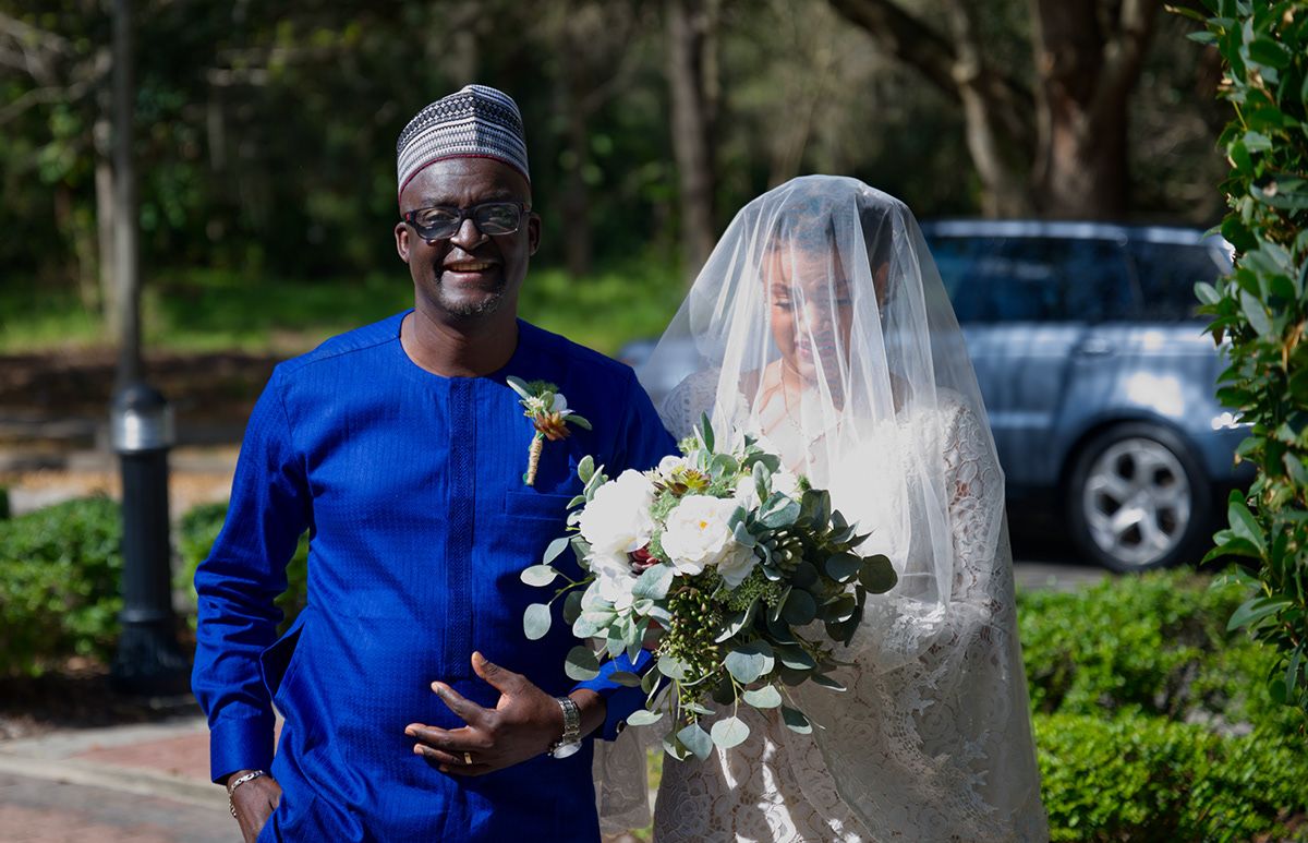 A wedding moment captured outdoors with a bouquet of white flowers and blue traditional attire.
