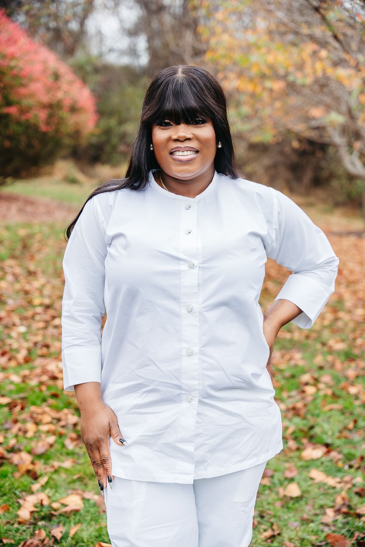 Person in crisp white button-down shirt poses outdoors among fall foliage.