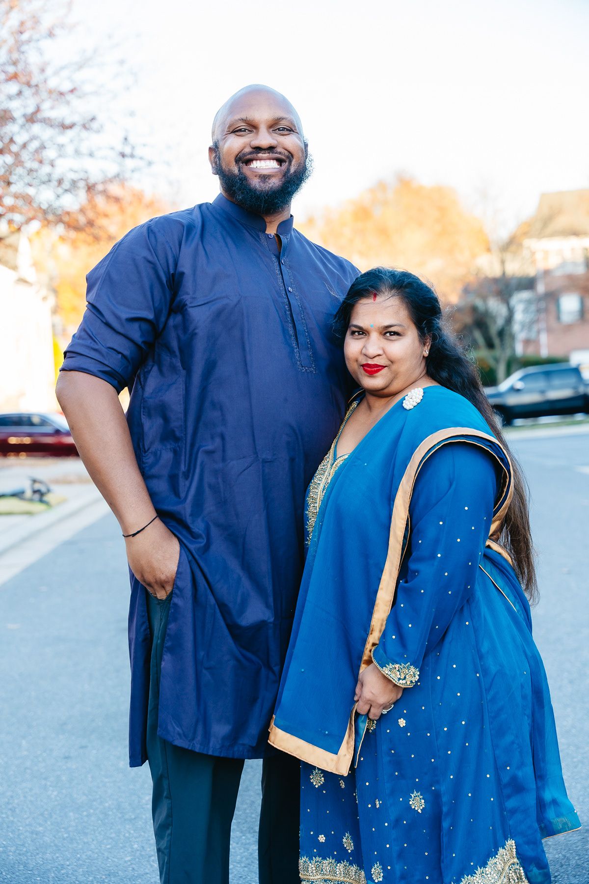 A couple poses outdoors wearing traditional South Asian formal attire in rich blue tones.