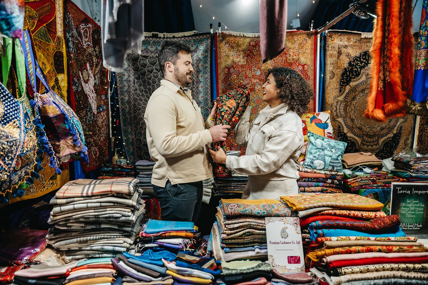 A couple shops together at a colorful market stall filled with textiles and fabrics.