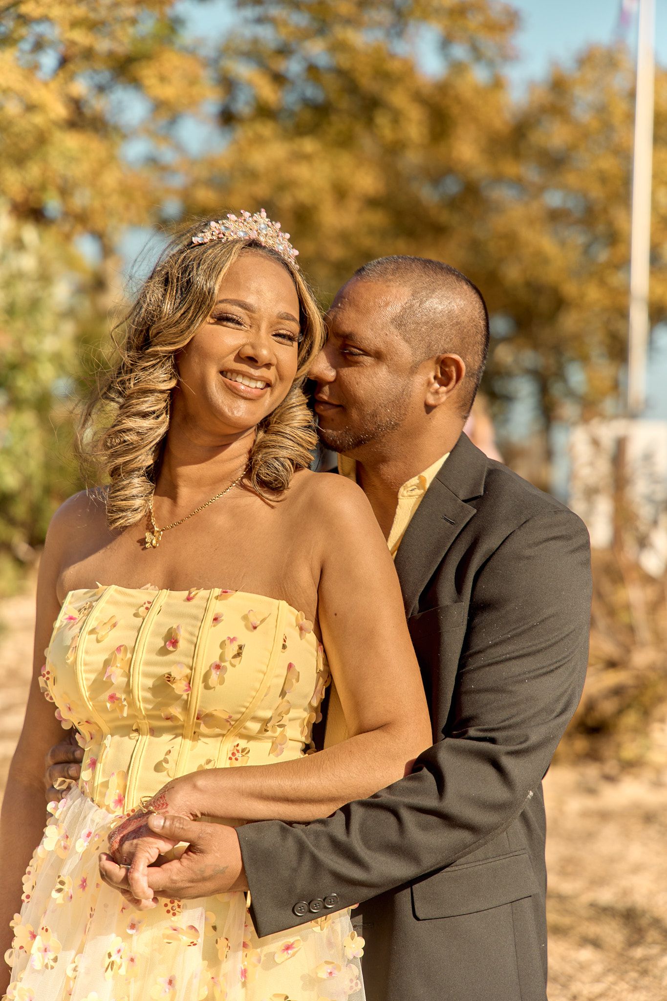 A romantic moment between a couple in formal attire with autumn trees behind them.