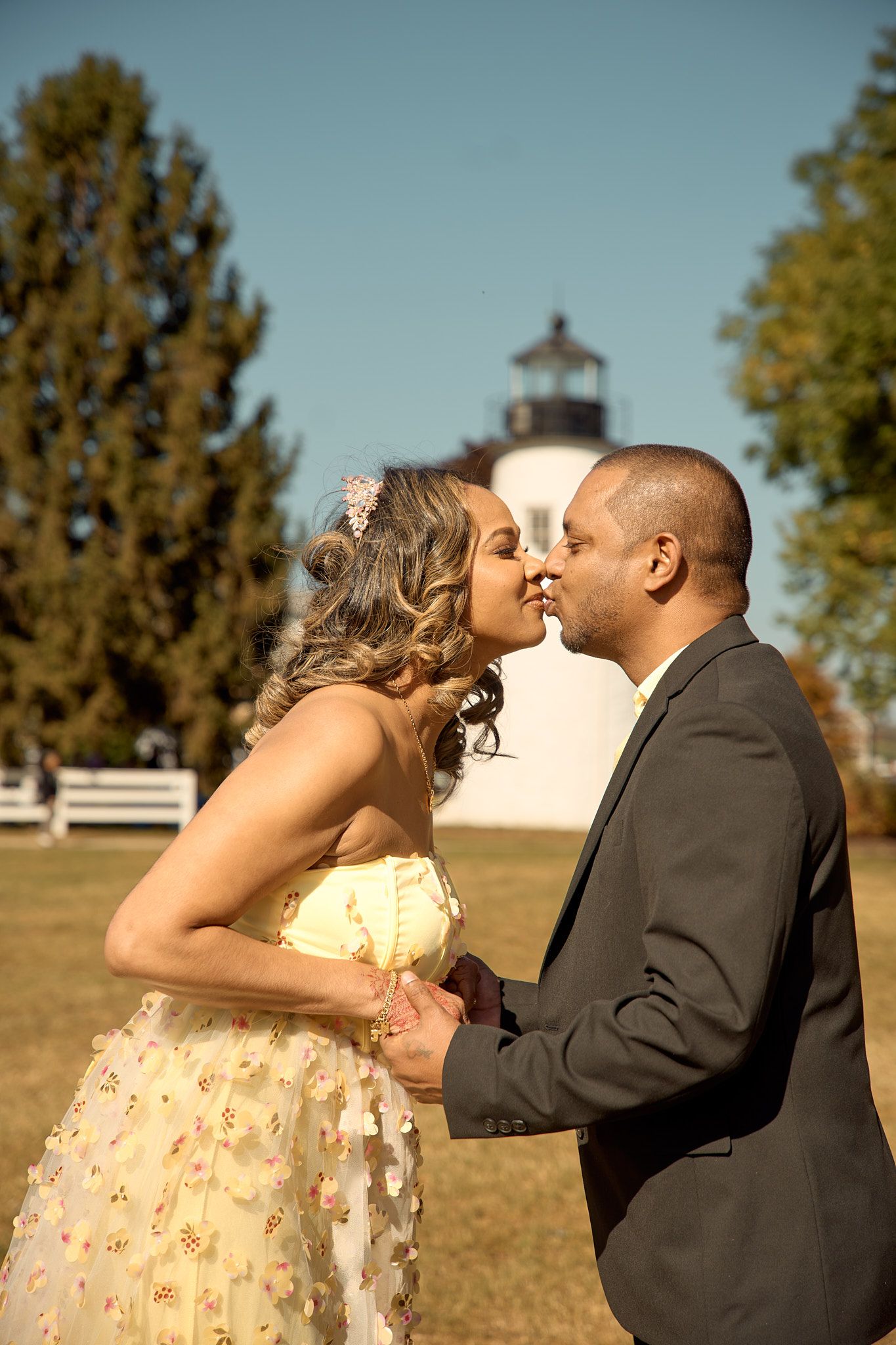 A romantic moment captured with a lighthouse and white fence in the background.