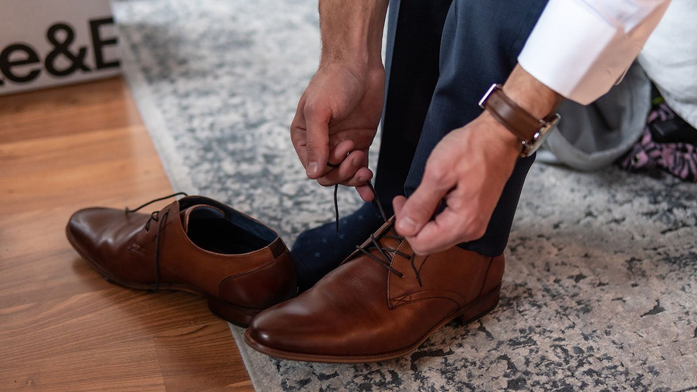 Close-up of hands tying brown leather dress shoes on a patterned carpet.