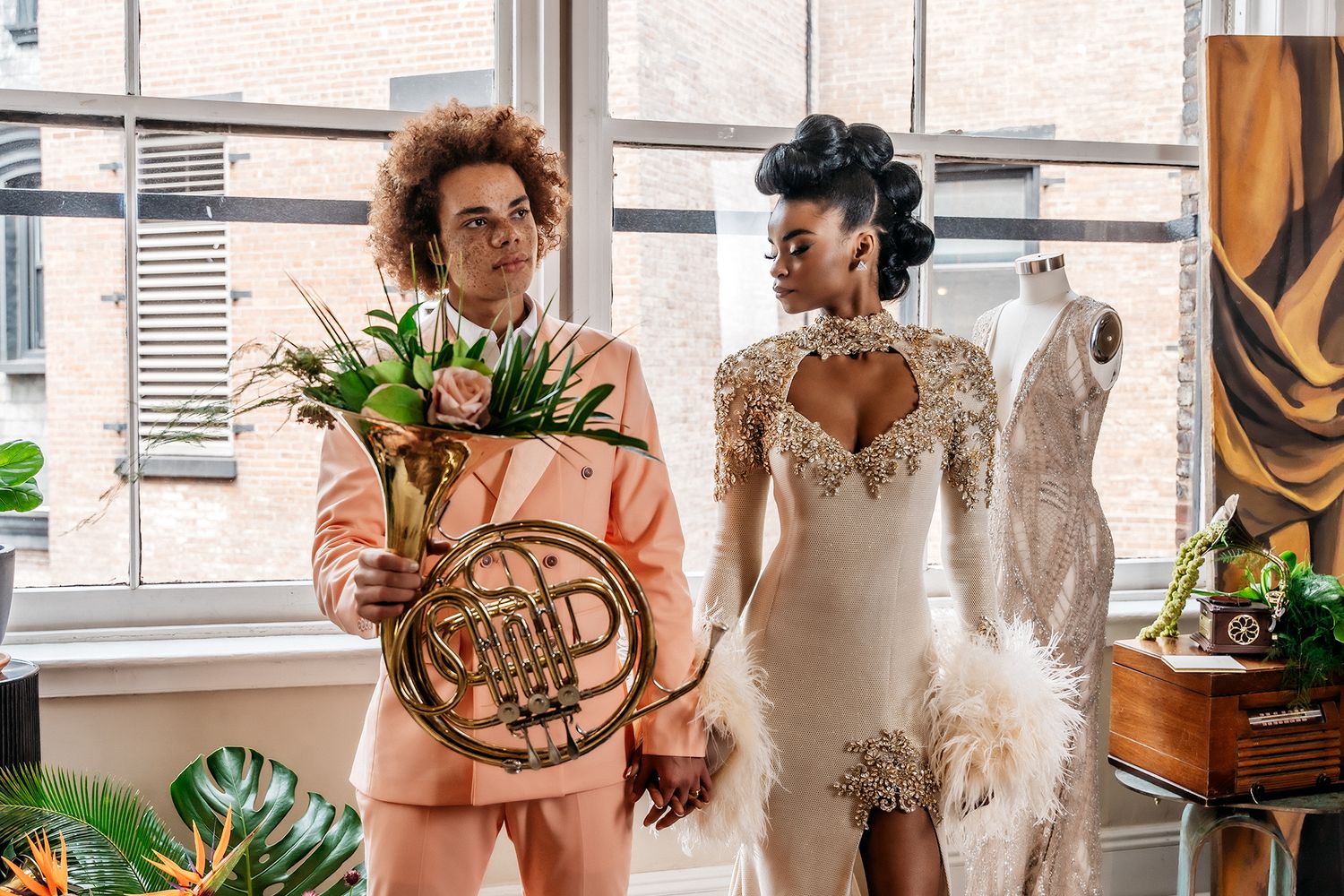 Two people in a bright room, one holding tulips with a French horn, the other wearing an elegant white dress.