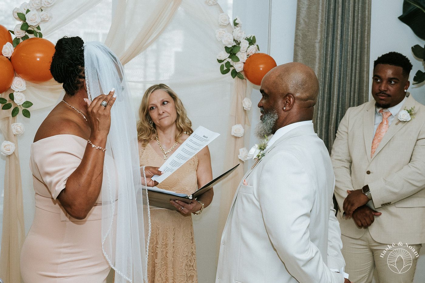 Wedding ceremony in progress with orange balloon decorations and officiant.