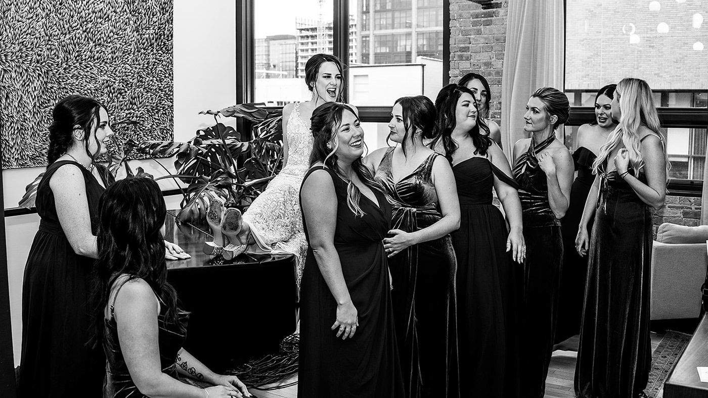 A group in black bridesmaid dresses gather for a candid moment at a wedding.