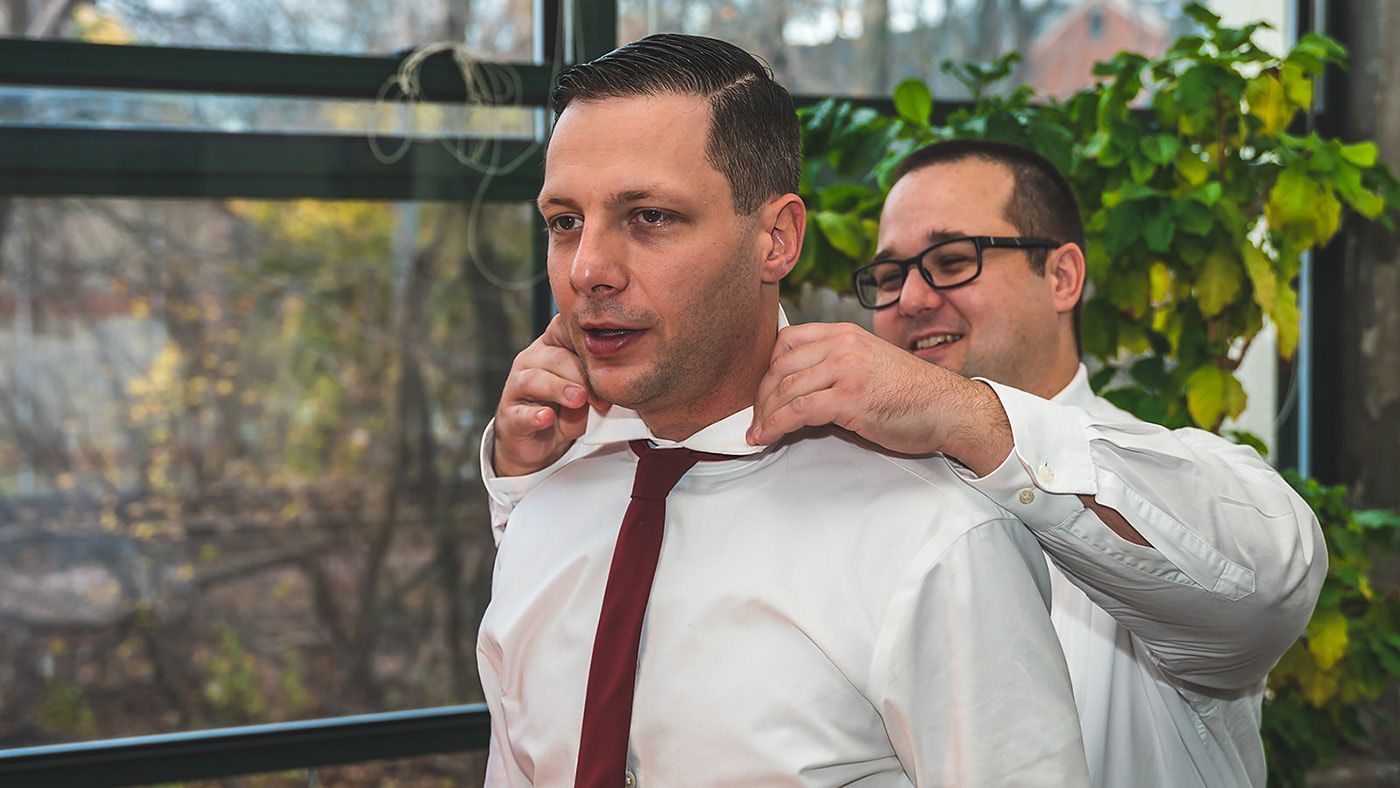 A groom gets help adjusting his tie while getting ready for the wedding ceremony.