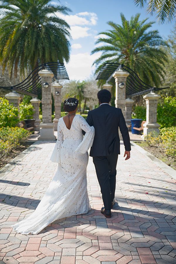 Newlyweds walking down palm-lined pathway at elegant venue after ceremony.