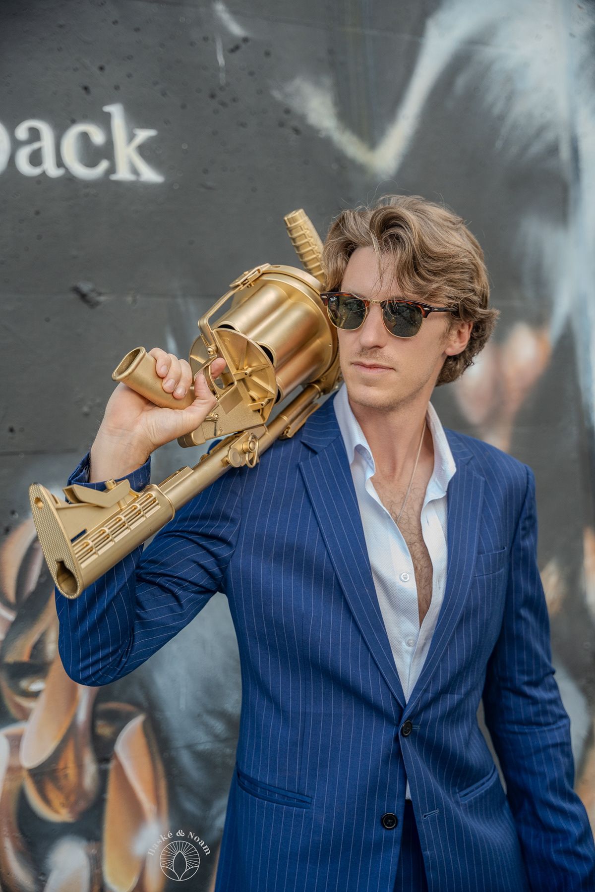 Model in pinstripe suit poses with gold prop against urban graffiti wall.