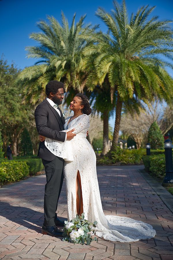 A romantic wedding couple posing on a brick pathway under towering palm trees.