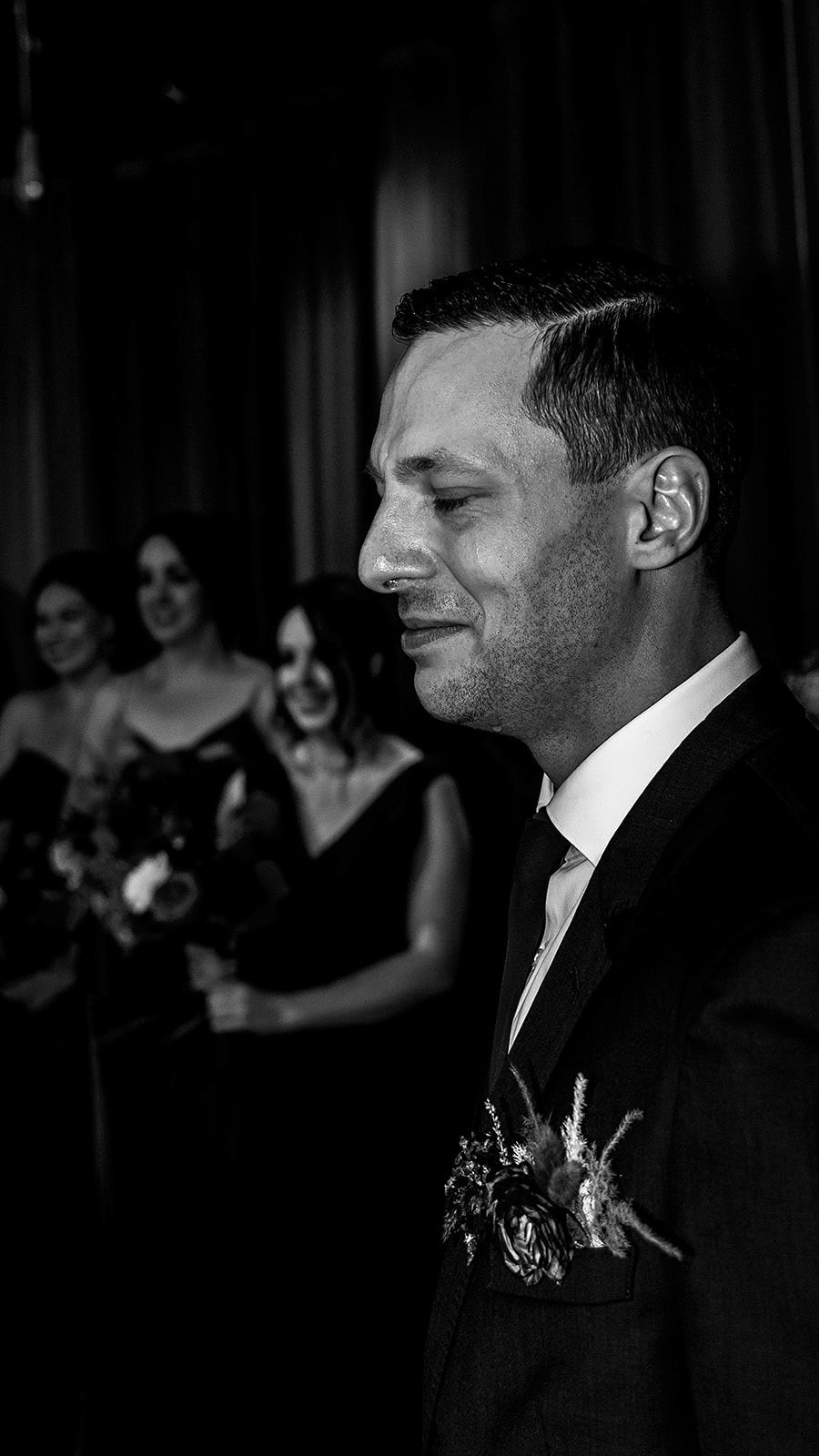Black and white portrait of groom wearing boutonniere and suit at wedding ceremony.