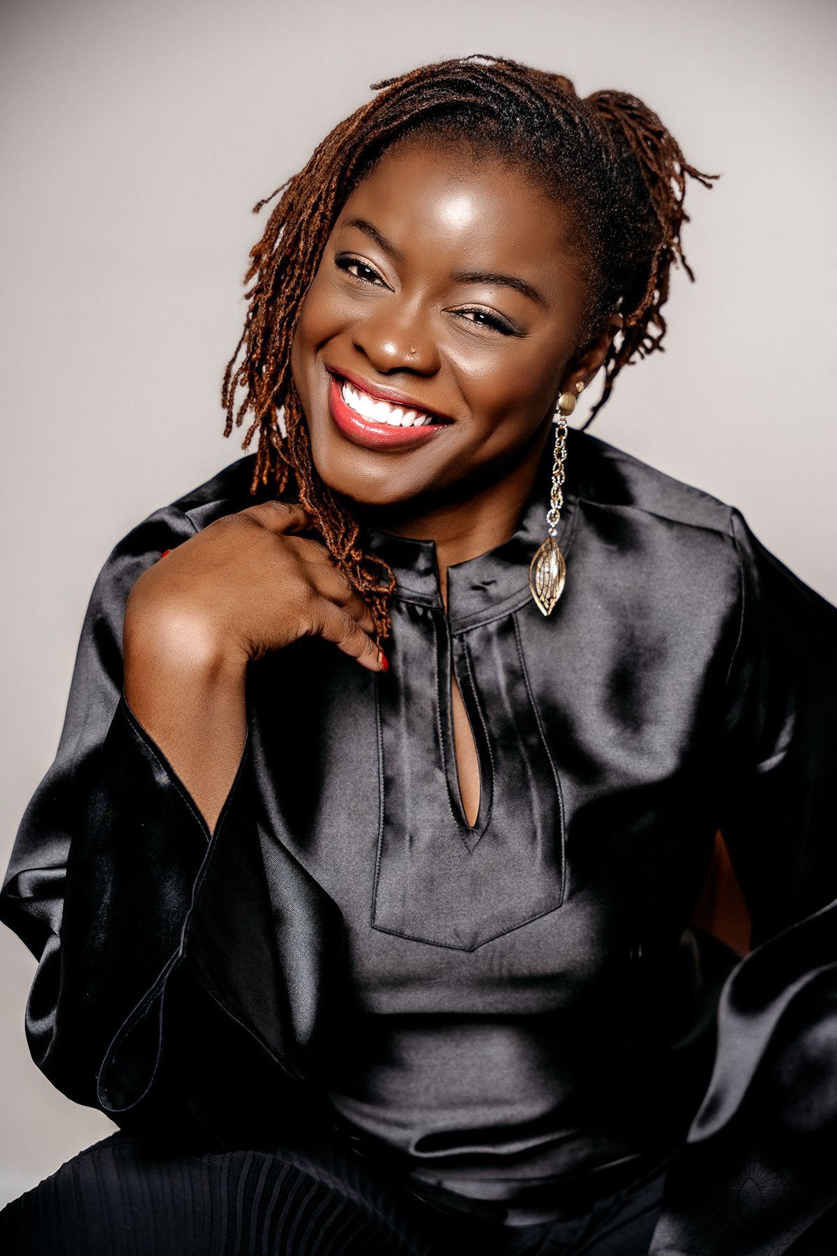Beautiful portrait of a person wearing a black satin top with locs and dazzling smile against neutral background.