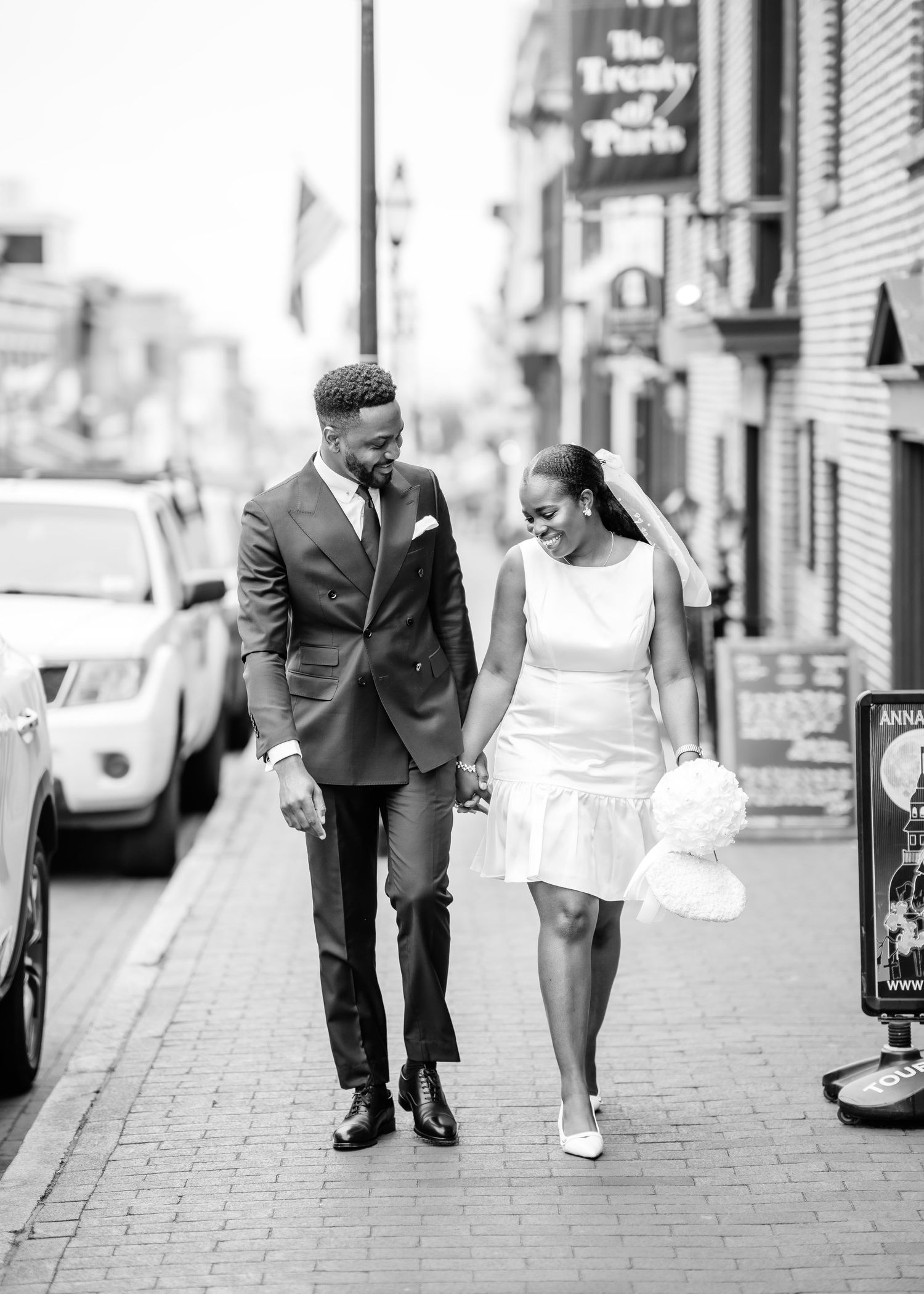 A couple in wedding attire walks down a city sidewalk together in black and white photography.