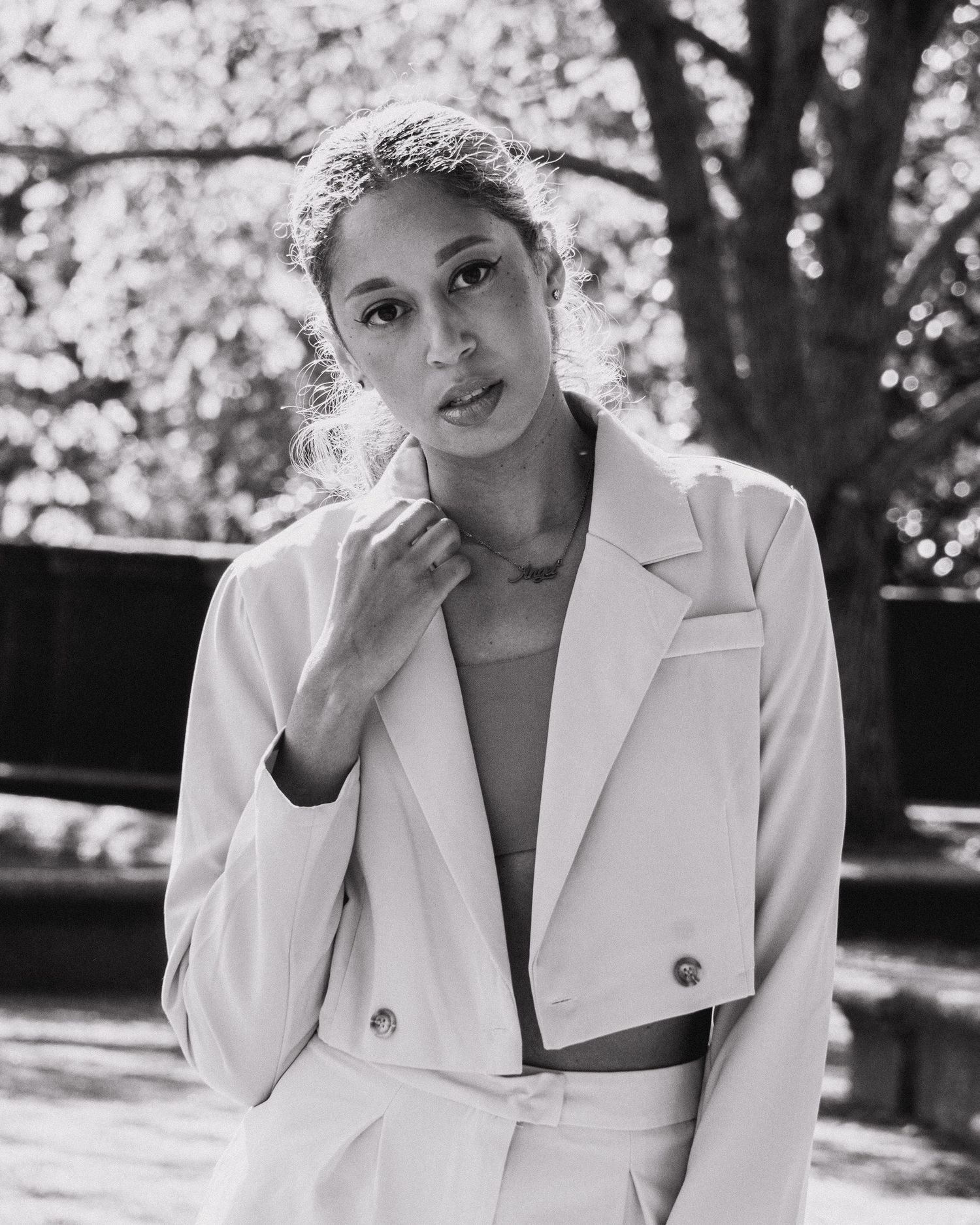 Professional portrait in white blazer captured in black and white against natural backdrop.