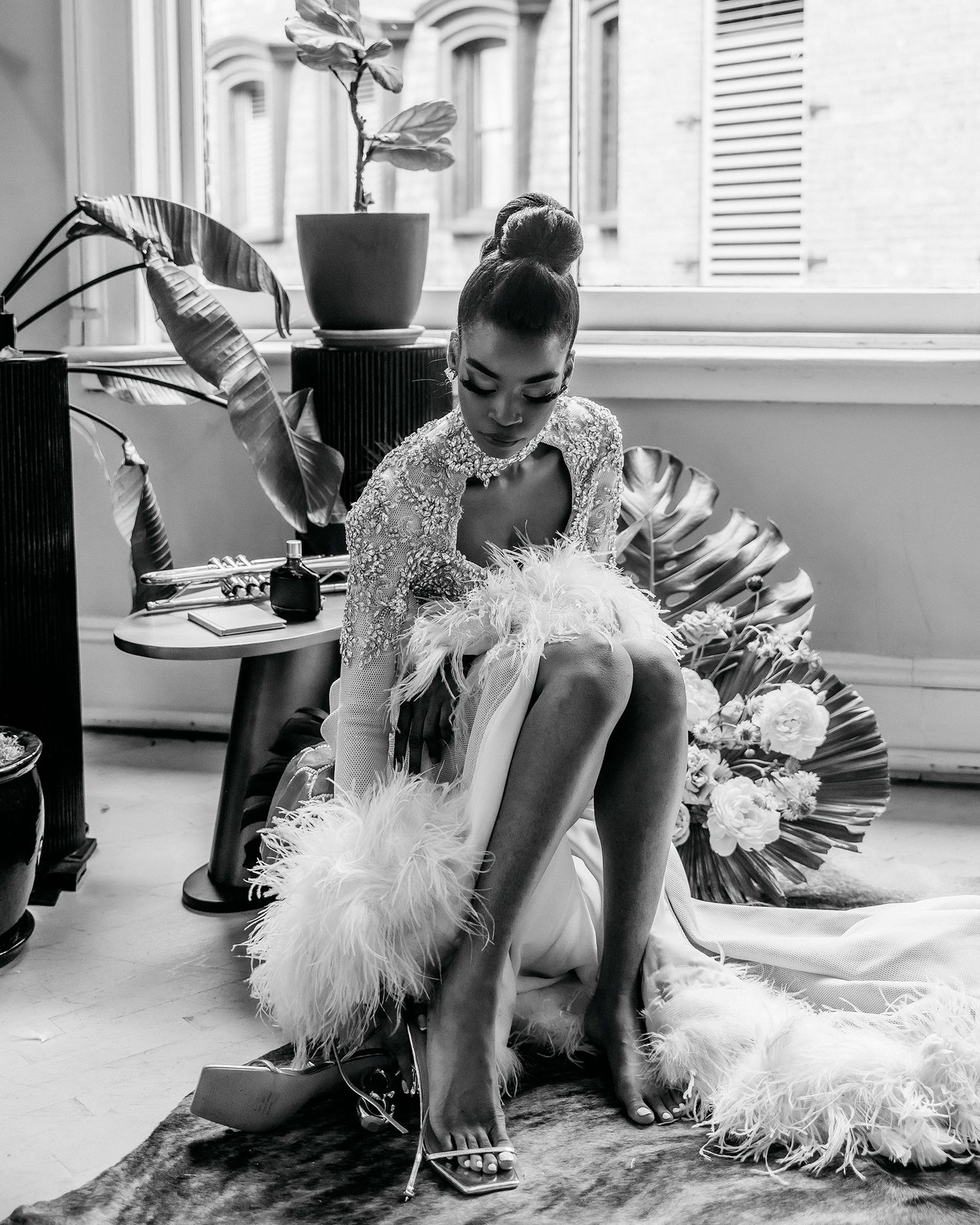 Black and white fashion photo featuring feathered dress and dramatic window lighting.